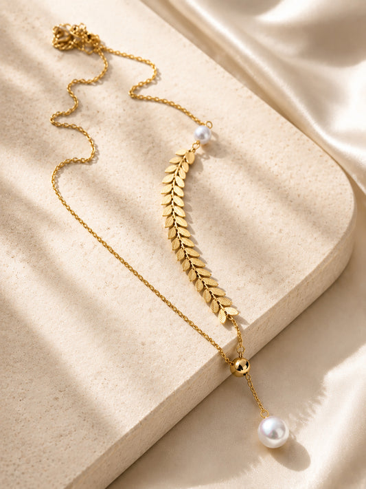 Elegant 18K gold-plated lariat necklace with a long leaf branch design and pearl accents displayed beautifully on stone and silk.