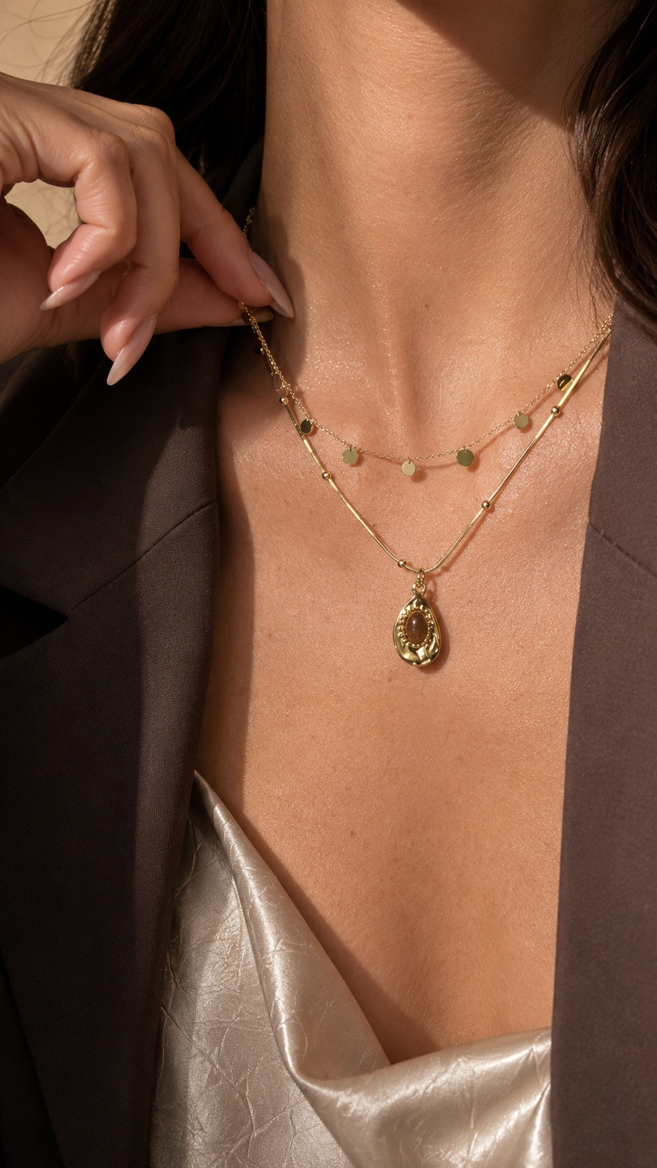 Model wrist touching neck showing double layer gold disc sequin chain and resin tiger's eye drop pendant