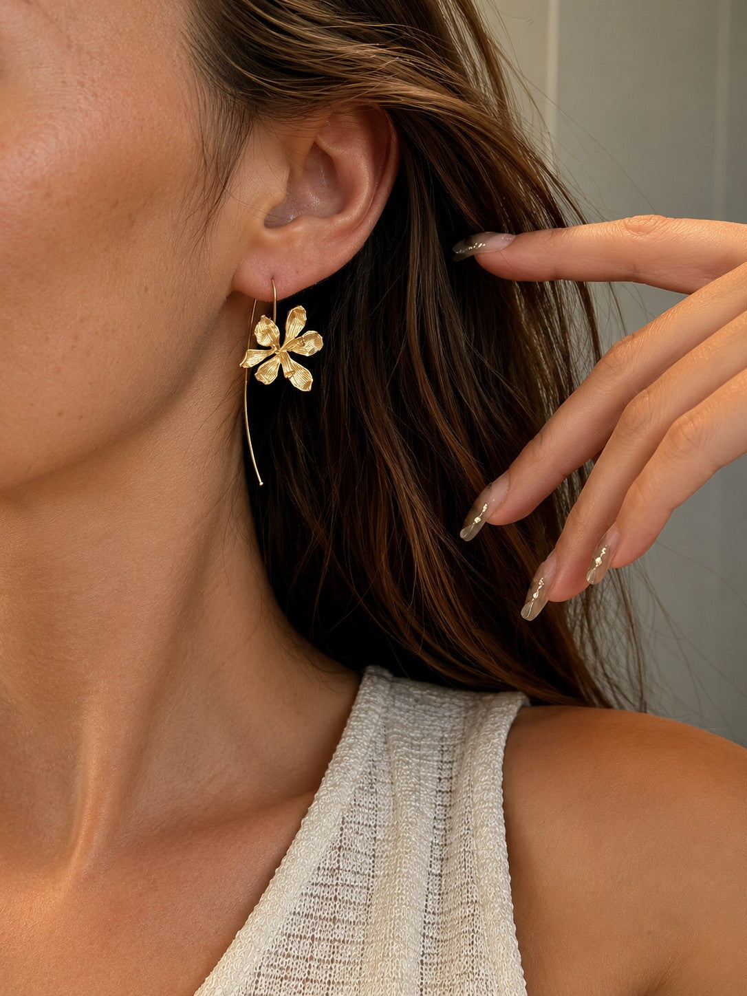 Close up of model touching hair showcasing textured gold botanical orchid wire hook drop earrings