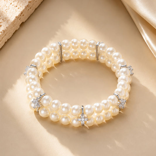 Classic double-row pearl bracelet with sparkling zirconia resting on textured stone and warm silk.