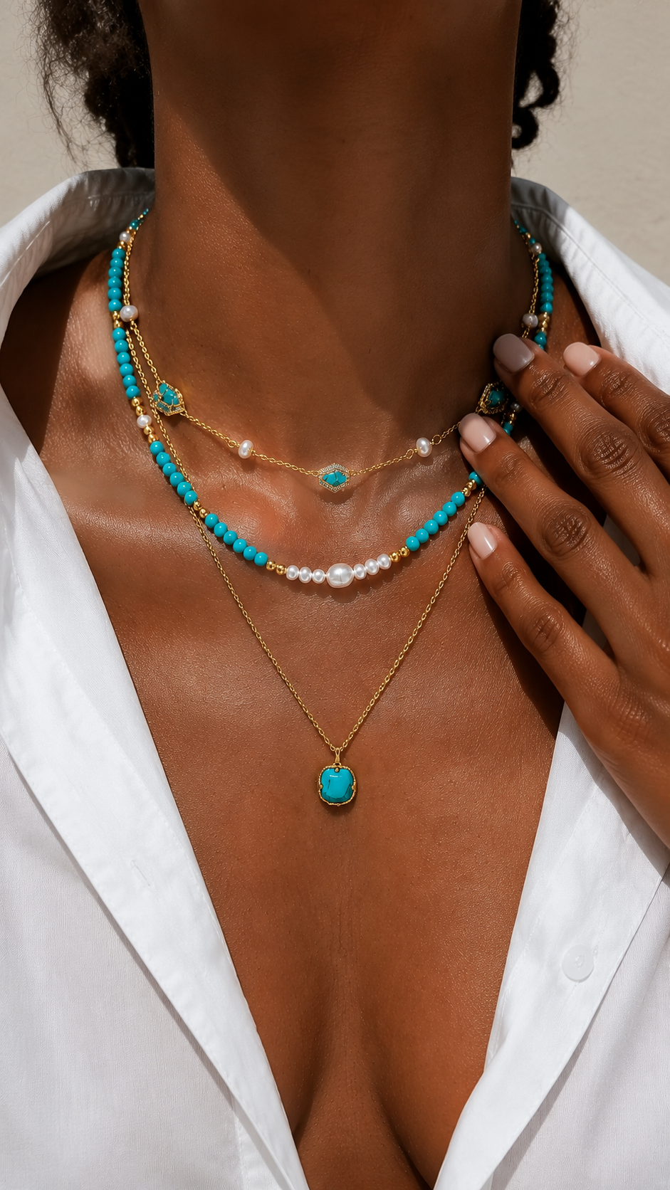 Close-up of a sun-kissed woman's décolletage showcasing a vibrant layered gold-tone necklace featuring turquoise stones and pearl accents.