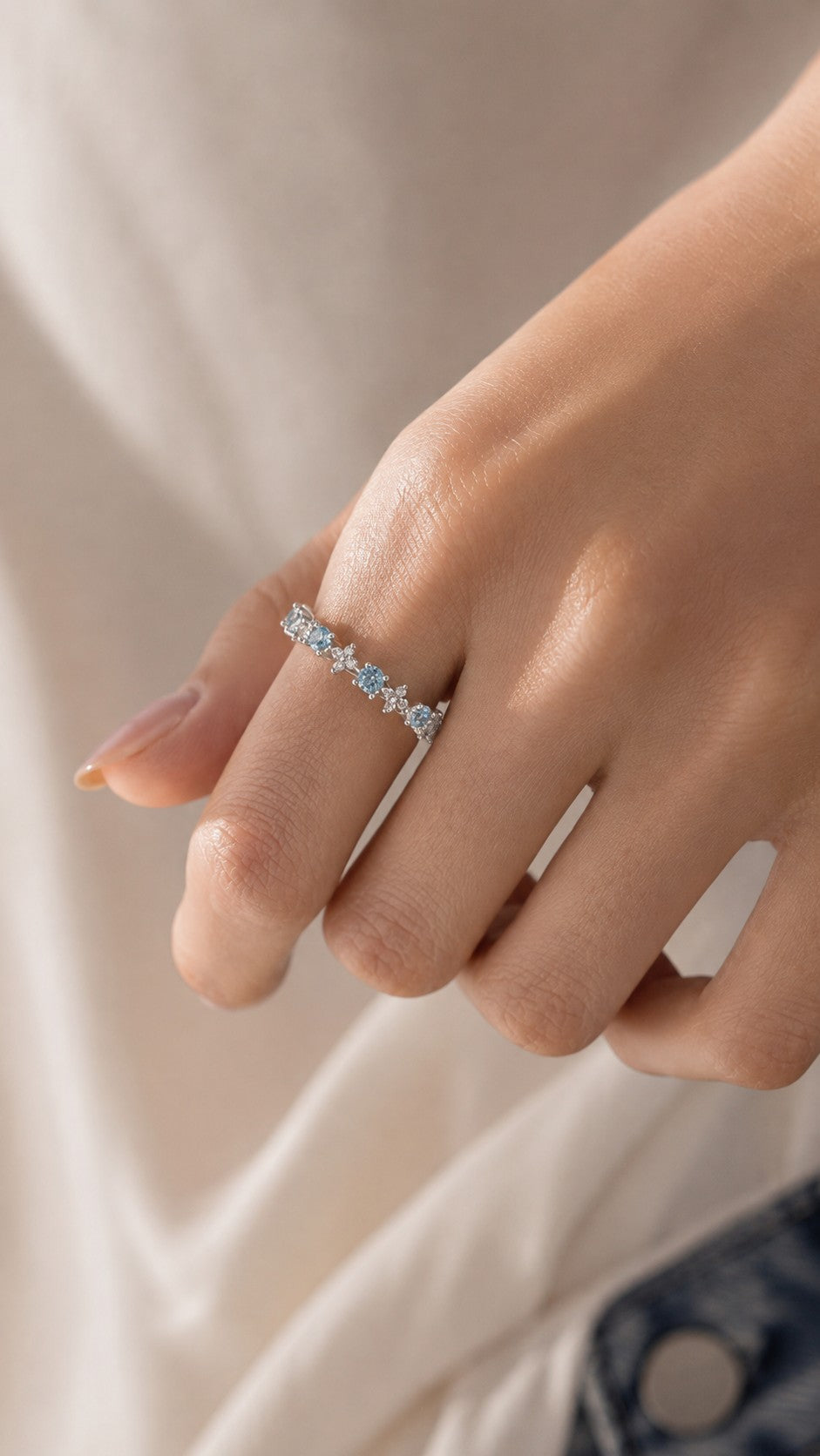 Close-up of model hand showcasing delicate aquamarine blue cz floral adjustable ring under warm natural sunlight