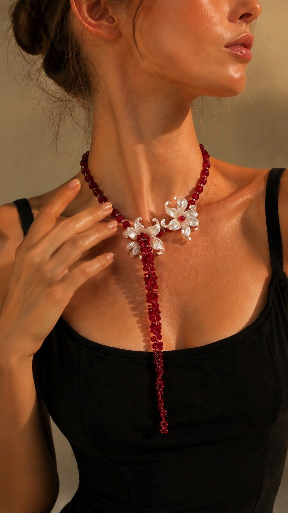 Close-up of a sun-kissed woman showcasing a bold red beaded choker necklace with twin white iris flowers and a long cascading tassel.