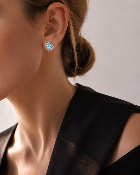 Confident woman wearing striking blue zirconia halo stud earrings and an elegant black dress.