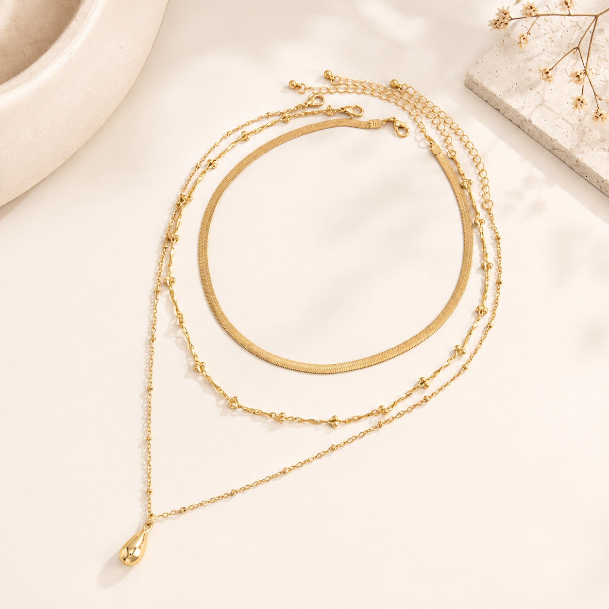 Gold layered necklace set styled on travertine stone plate with dry flowers