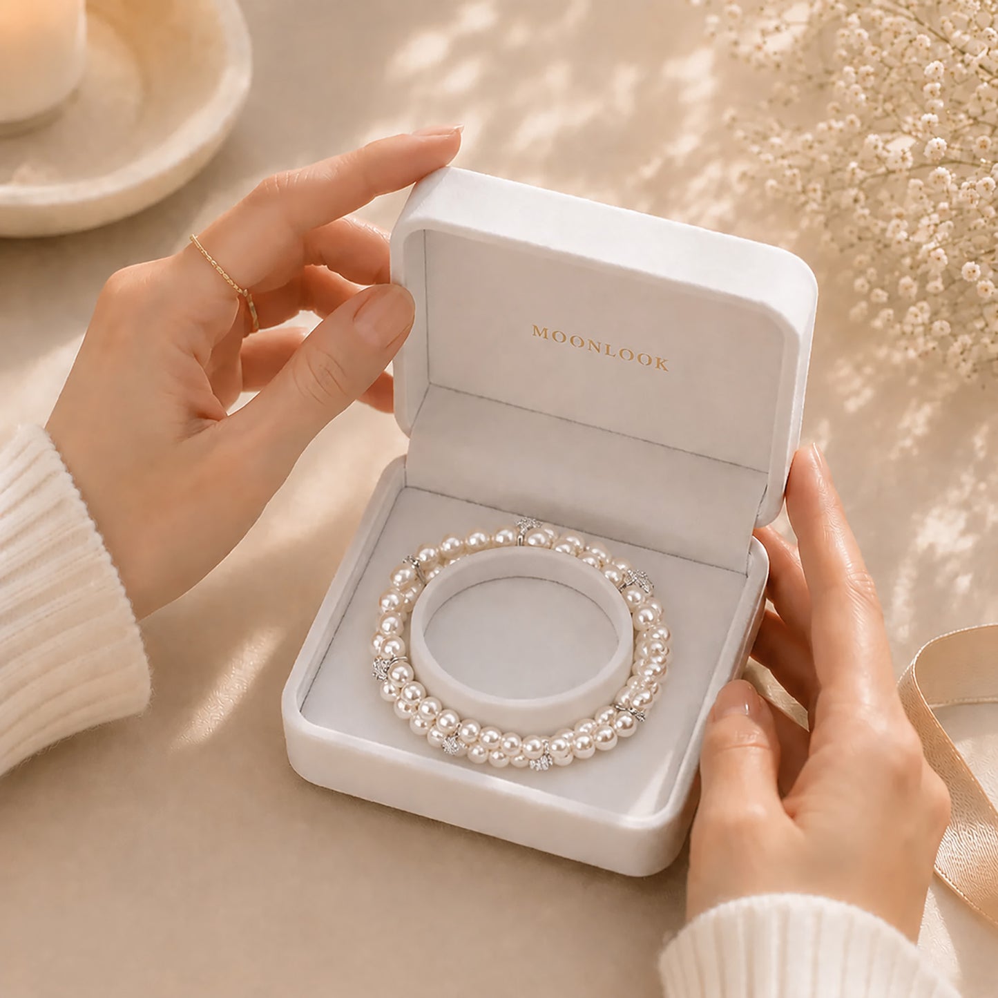 Hands gently opening a white Moonlook gift box revealing a beautiful double-layer pearl bracelet.