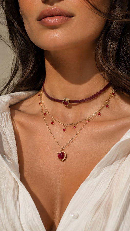 Close up of model wearing burgundy leather choker and gold layered necklace with ruby red heart pendant
