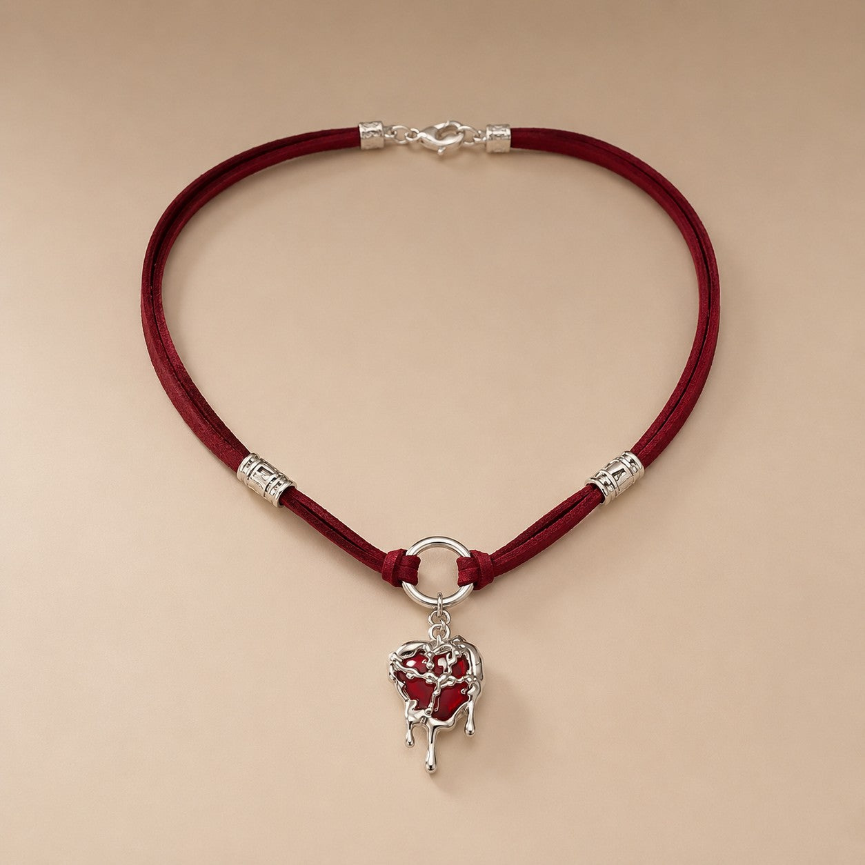Flatlay view of burgundy suede choker with silver molten liquid dripping heart pendant on beige background