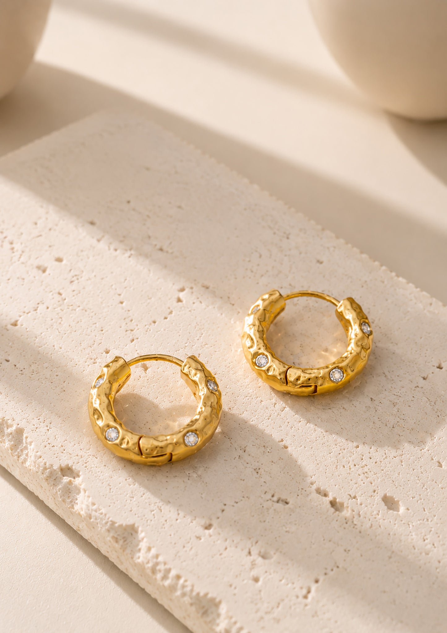 Pair of vintage-inspired hammered gold-tone hoop earrings resting beautifully on a textured aesthetic stone block.