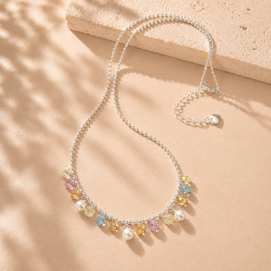 Beautiful rainbow colored zirconia and pearl fringe necklace displayed with soft shadows on a beige background.