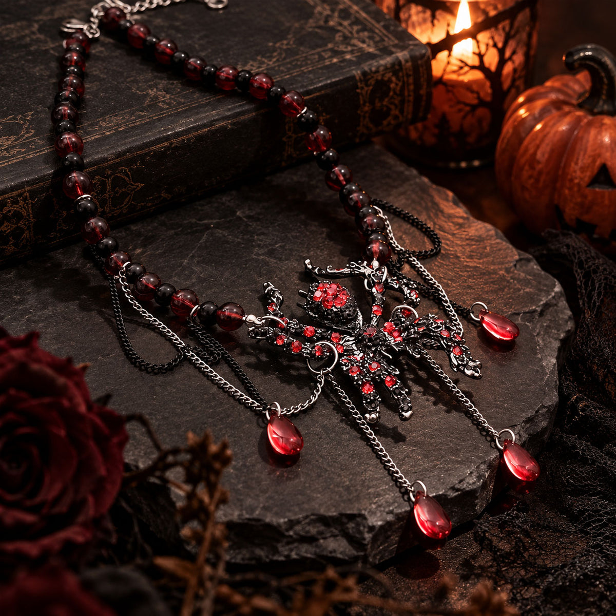 Flat lay of gothic crimson spider pendant necklace resting on antique book beside dark red roses
