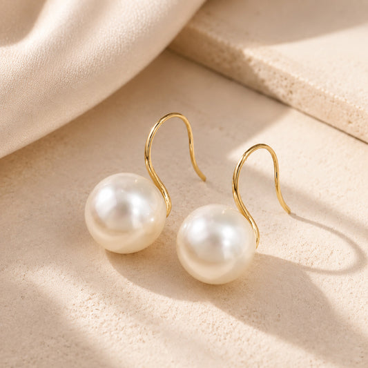 Close up of vintage-inspired 14K gold-plated french hook earrings with large white pearls resting on warm stone.