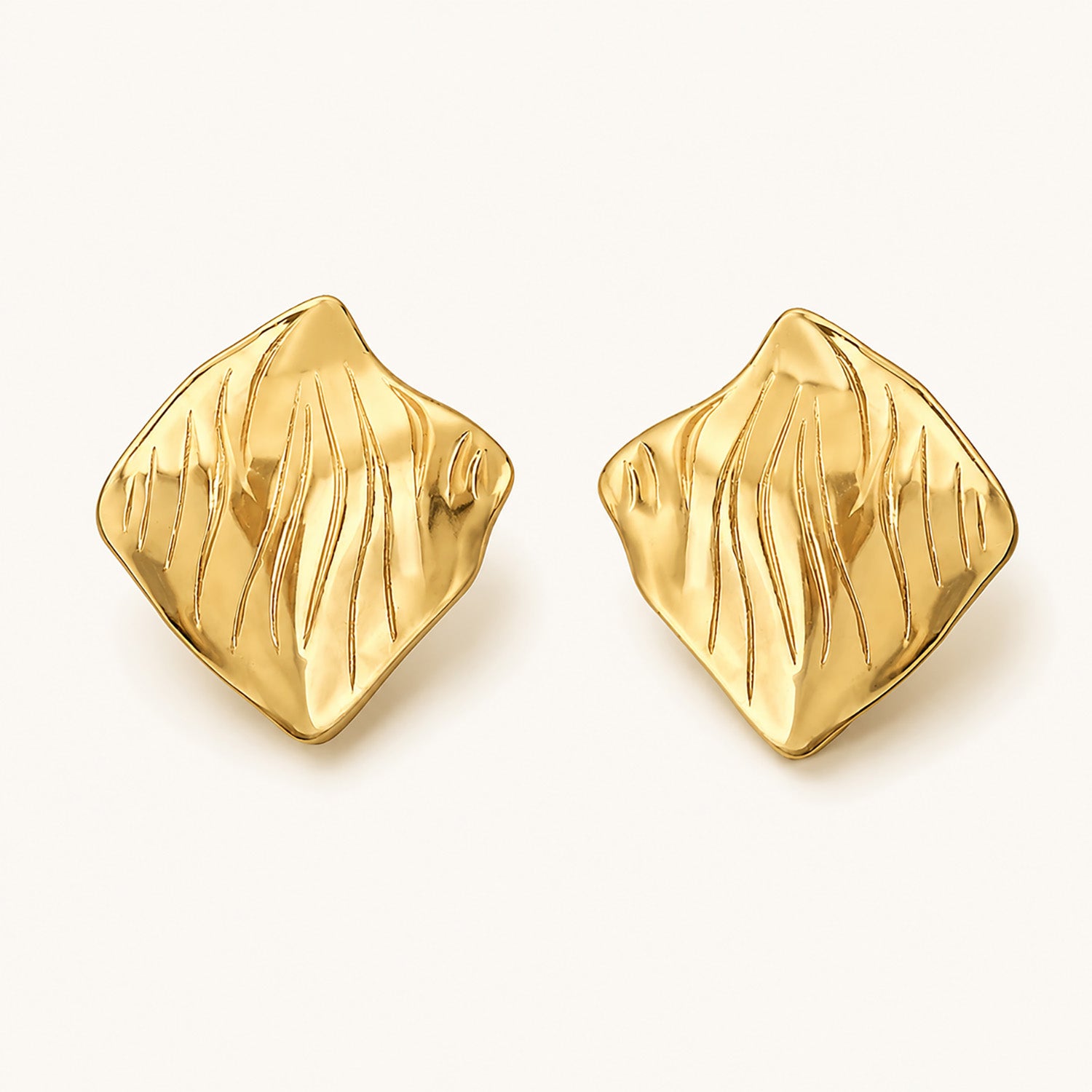 Minimalist flat lay of 18K gold-plated square stud earrings featuring an artistic crinkled surface on a clean white background.