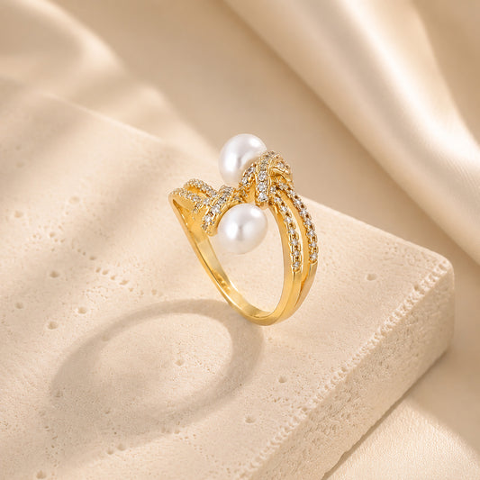 Elegant 18K gold-tone twisted rope bypass ring featuring micro-paved zircon knots and dual freshwater pearls on an aesthetic stone surface.