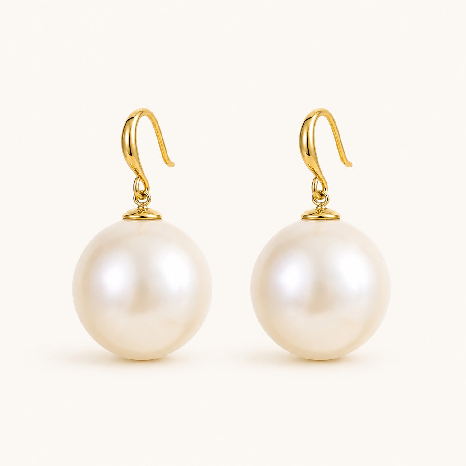 Minimalist flat lay of 14K gold-plated french hook earrings featuring massive 19mm statement pearls on a white background.
