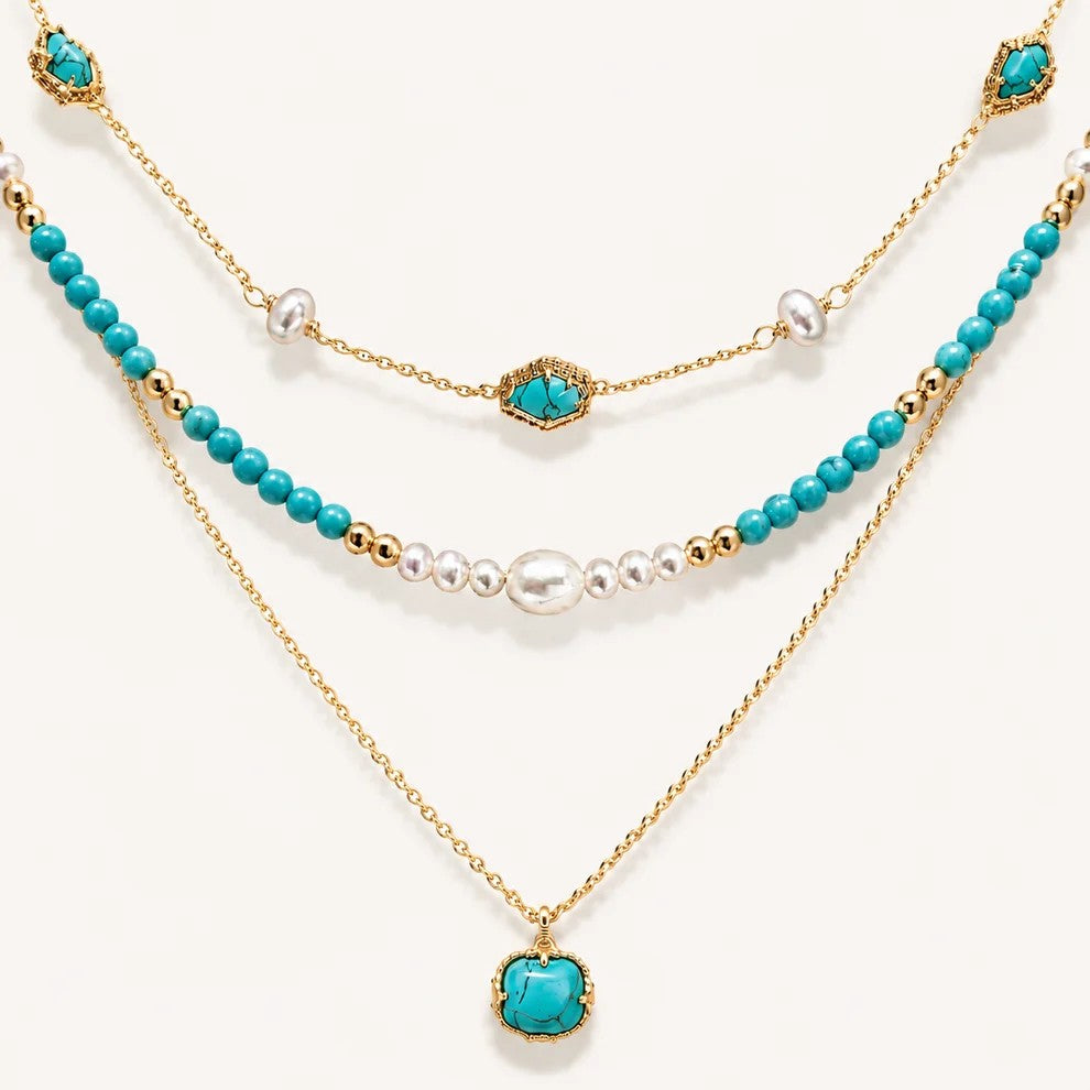 Detailed flat lay of a three-tier 22K gold-plated necklace featuring vibrant turquoise beads, genuine pearls, and a turquoise pendant on a white background.