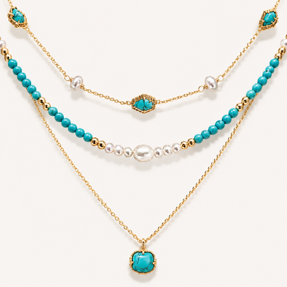 Detailed flat lay of a three-tier 22K gold-plated necklace featuring vibrant turquoise beads, genuine pearls, and a turquoise pendant on a white background.