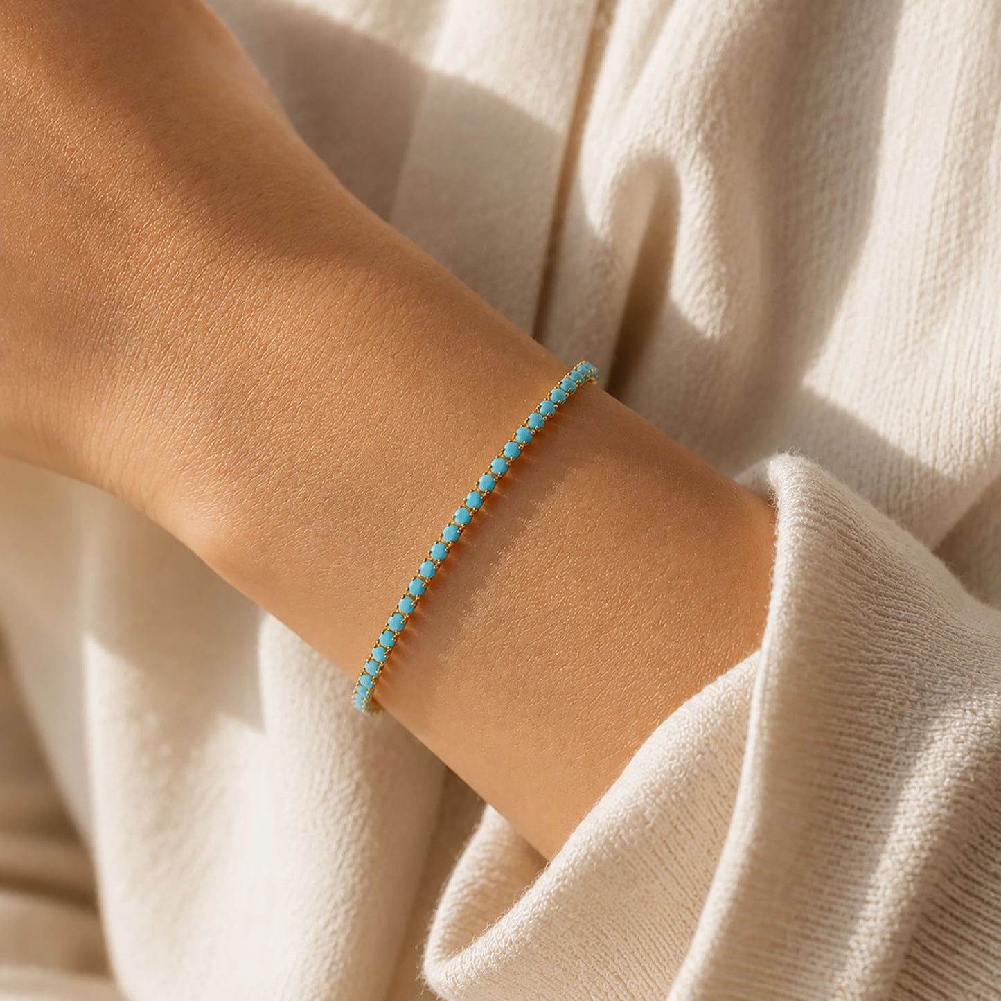 Close-up-look-of-a-minimalist-gold-turquoise-bracelet-styled-on-a-woman-wrist-with-a-cozy-white-sweater