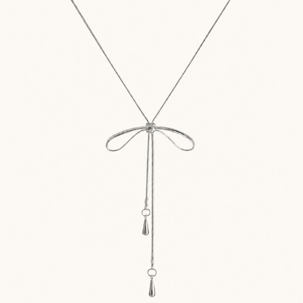 Minimalist flat lay of a silver-tone bolo necklace featuring a bow motif and long adjustable snake chain drops on a white background.