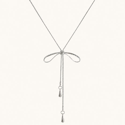 Minimalist flat lay of a silver-tone bolo necklace featuring a bow motif and long adjustable snake chain drops on a white background.