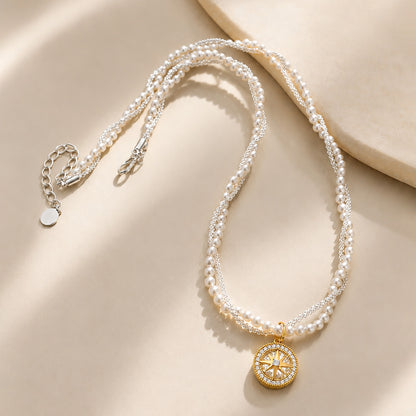 Vintage-inspired compass star necklace with intertwined pearls and gold-tone chain resting gracefully on a textured stone surface.