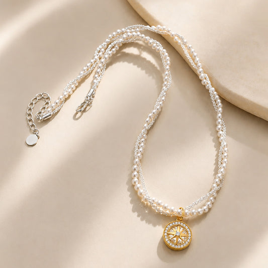 Vintage-inspired compass star necklace with intertwined pearls and gold-tone chain resting gracefully on a textured stone surface.