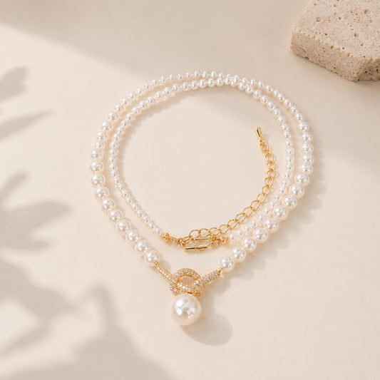 Elegant 18K gold-tone knotted pearl pendant necklace displayed with soft leaf shadows on a textured background.