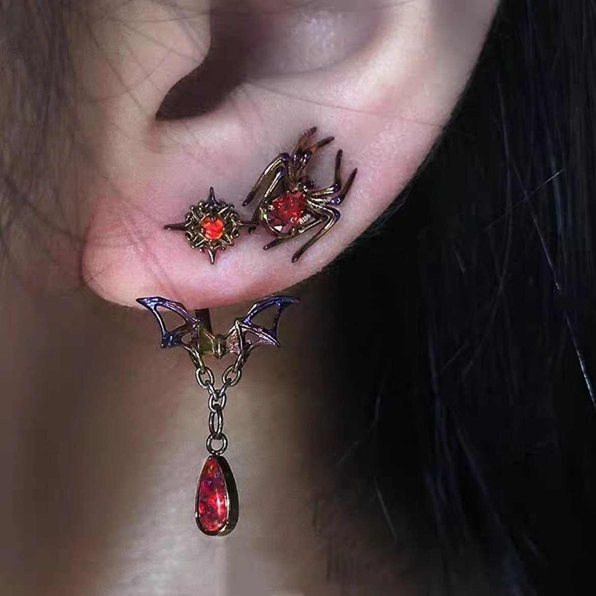Model wearing matching asymmetric gothic spider stud and dangling bat wing ear jacket on earlobe