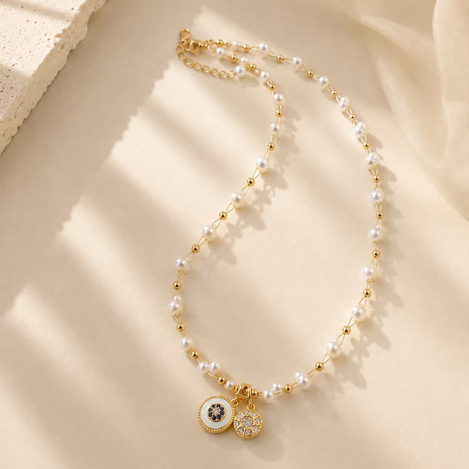 Elegant pearl and gold-tone beaded necklace with vintage double disc pendants on a textured surface.
