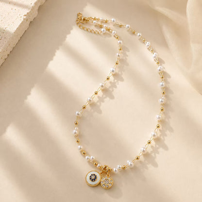 Elegant pearl and gold-tone beaded necklace with vintage double disc pendants on a textured surface.