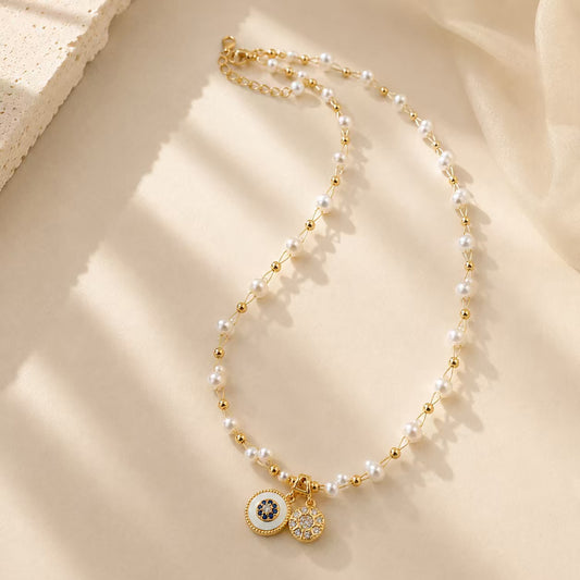 Elegant pearl and gold-tone beaded necklace with vintage double disc pendants on a textured surface.