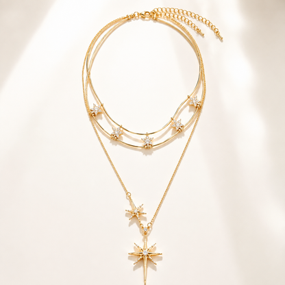 Minimalist flat lay of a complex layered gold-tone necklace featuring a double-wire choker with mini stars and a long sunburst pendant on a white background.