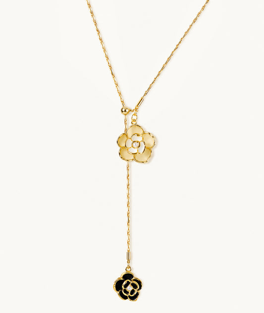 Minimalist flat lay of an gold-plated Y-necklace featuring black and white camellia flower pendants and delicate pearl accents on a white background.
