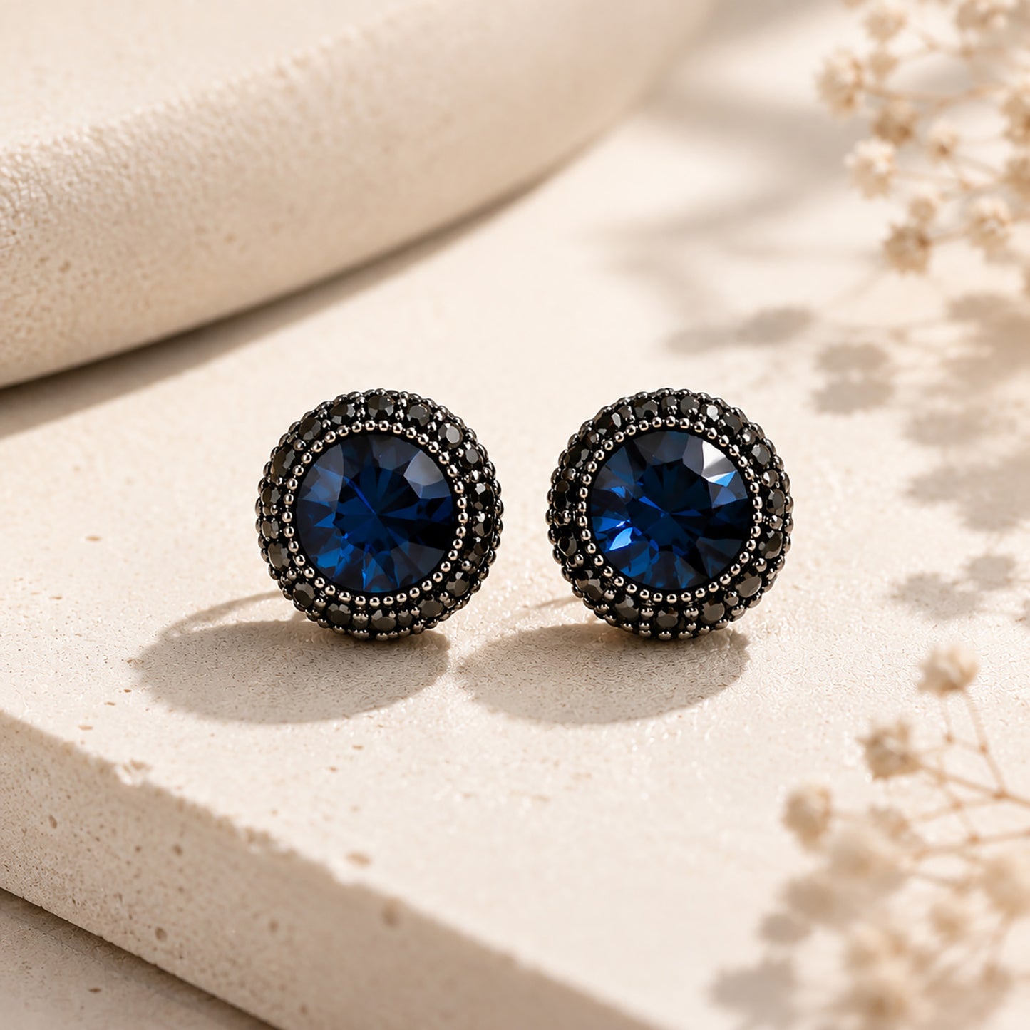 Elegant black zirconia halo stud earrings resting on a warm, textured stone surface.