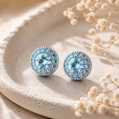 Close-up of elegant blue round zirconia stud earrings resting in a minimalist stone tray.