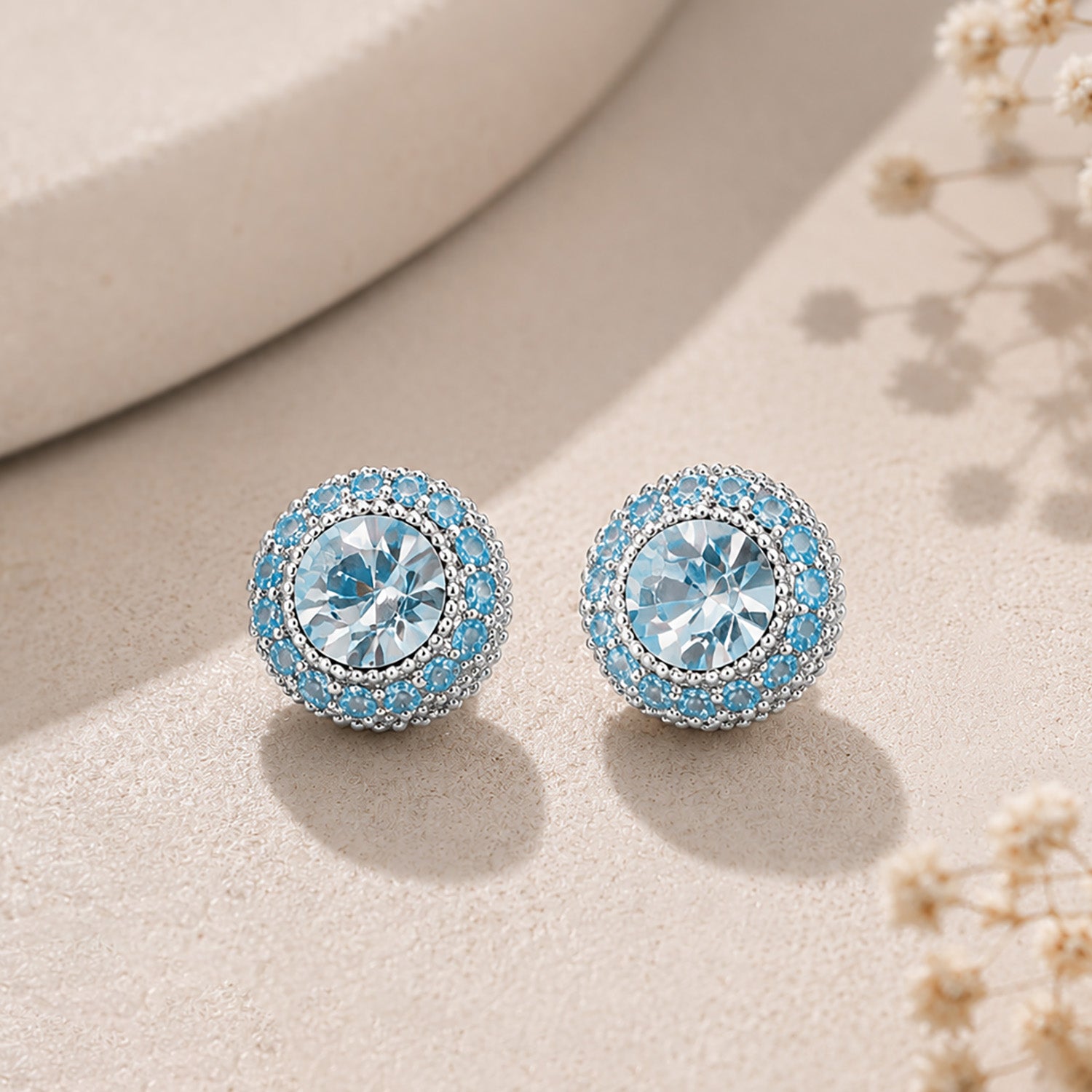 Dazzling sapphire blue halo stud earrings displayed elegantly on a textured aesthetic stone.