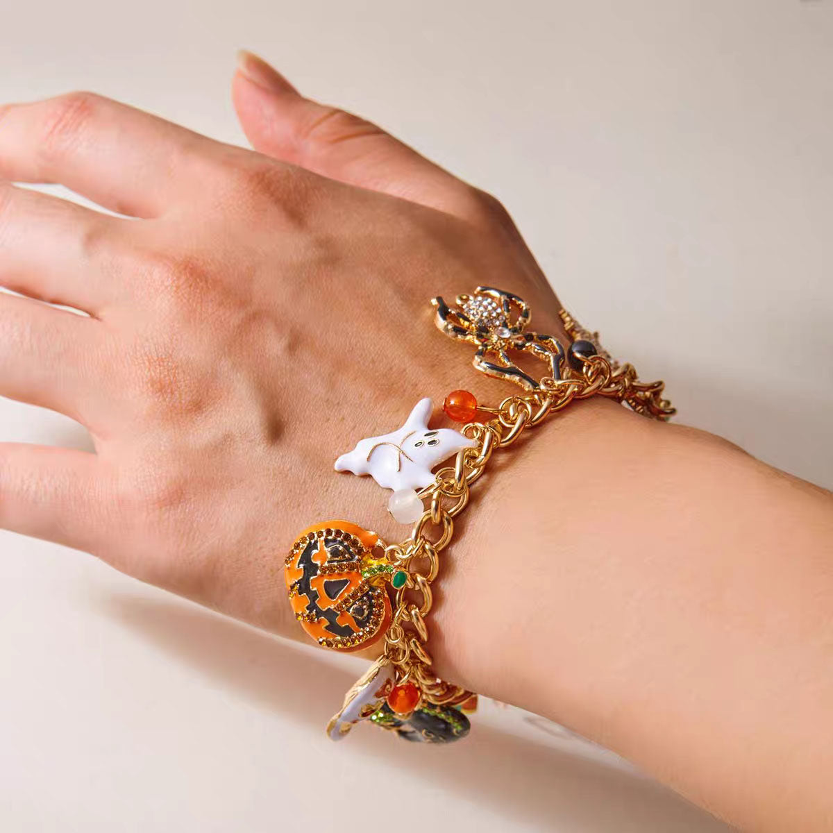 Close-up of hand wearing gold Halloween charm bracelet with pumpkin, ghost, and spider charms