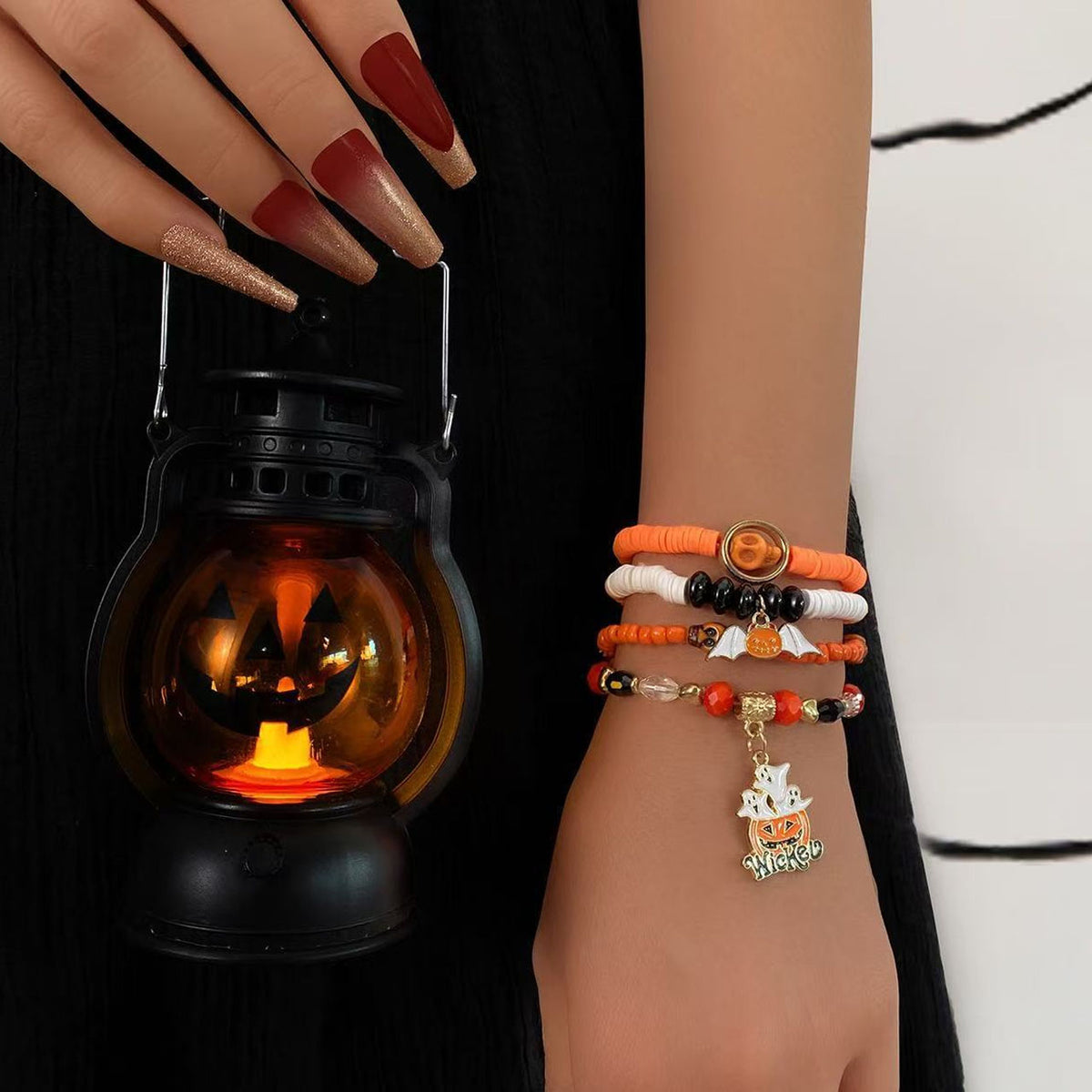 Model wearing orange and black Halloween stackable clay bead bracelets holding a glowing jack-o-lantern