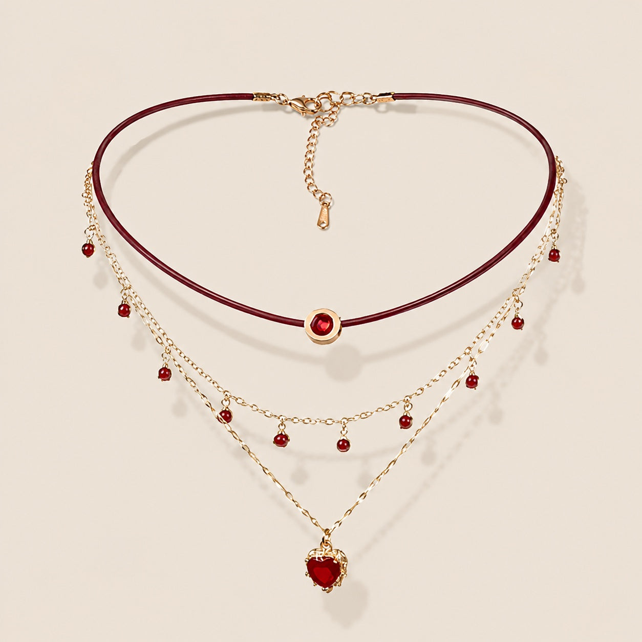 Flatlay view of triple layered burgundy leather choker necklace with gold chain and ruby red heart pendant