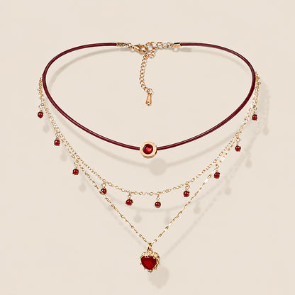 Flatlay view of triple layered burgundy leather choker necklace with gold chain and ruby red heart pendant