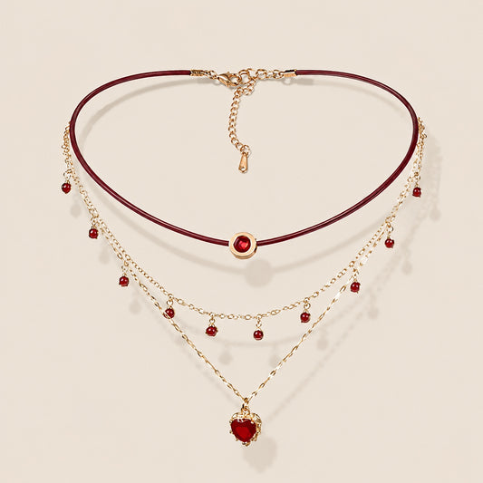 Flatlay view of triple layered burgundy leather choker necklace with gold chain and ruby red heart pendant