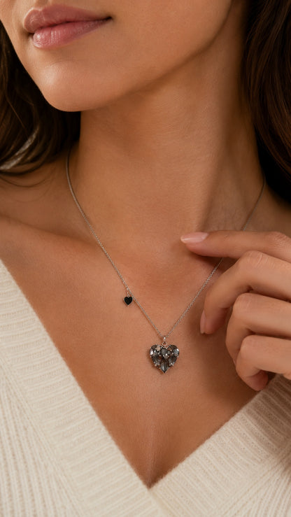 Close up of model touching collarbone showing black CZ heart pendant necklace with side charm accent