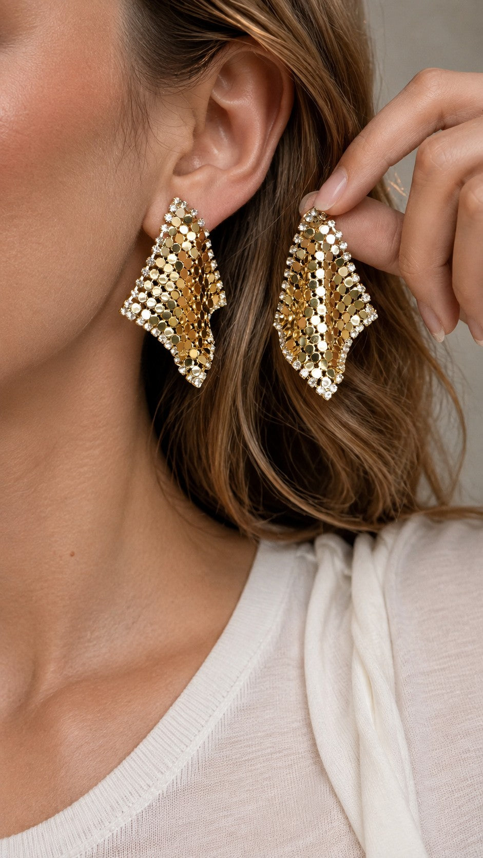 Model holding up a sparkling 4.3cm gold liquid metal mesh scarf stud earring next to ear