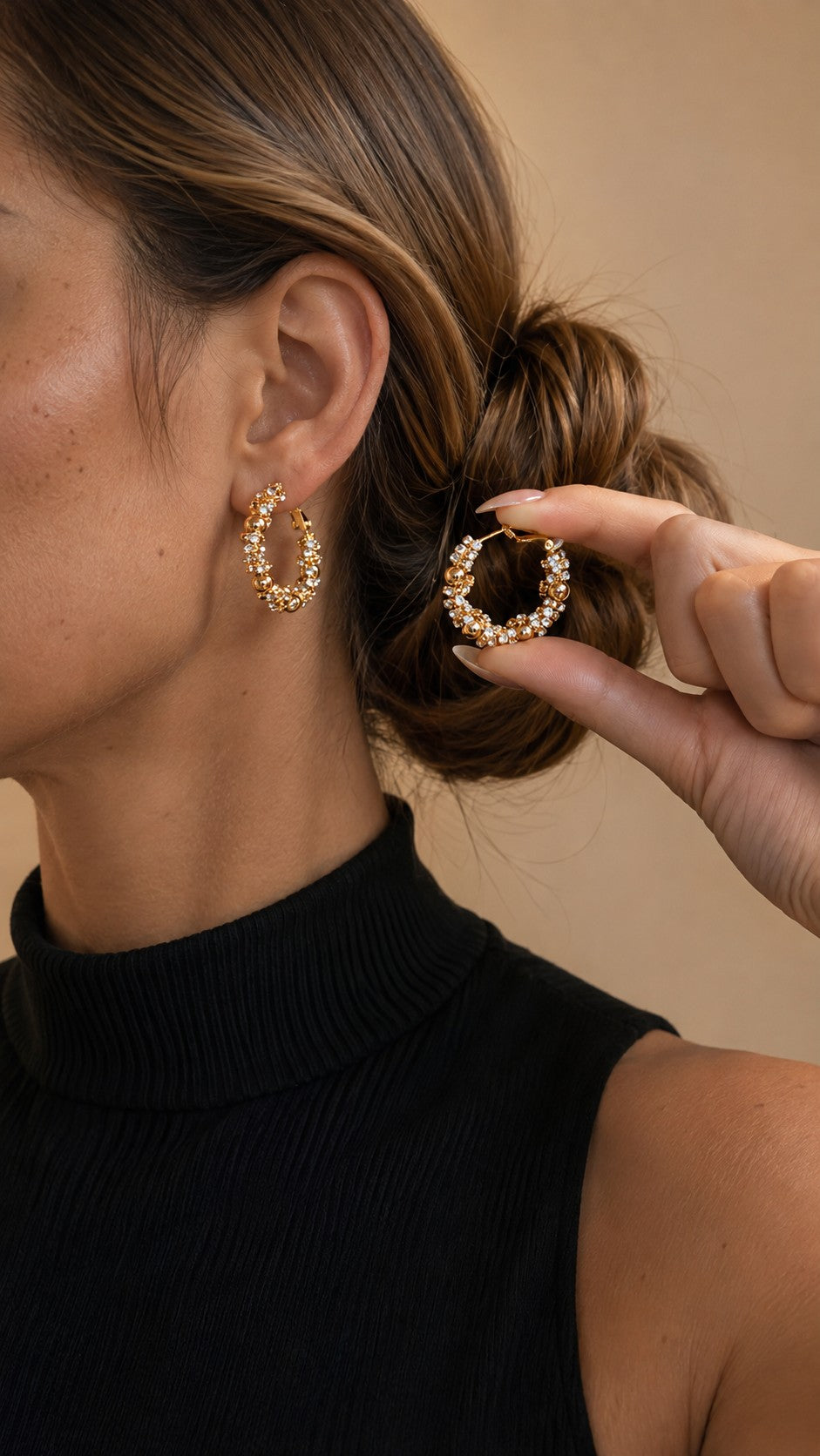 Close up of model holding up a textured 2.8cm gold bead pave crystal cluster hoop earring next to ear