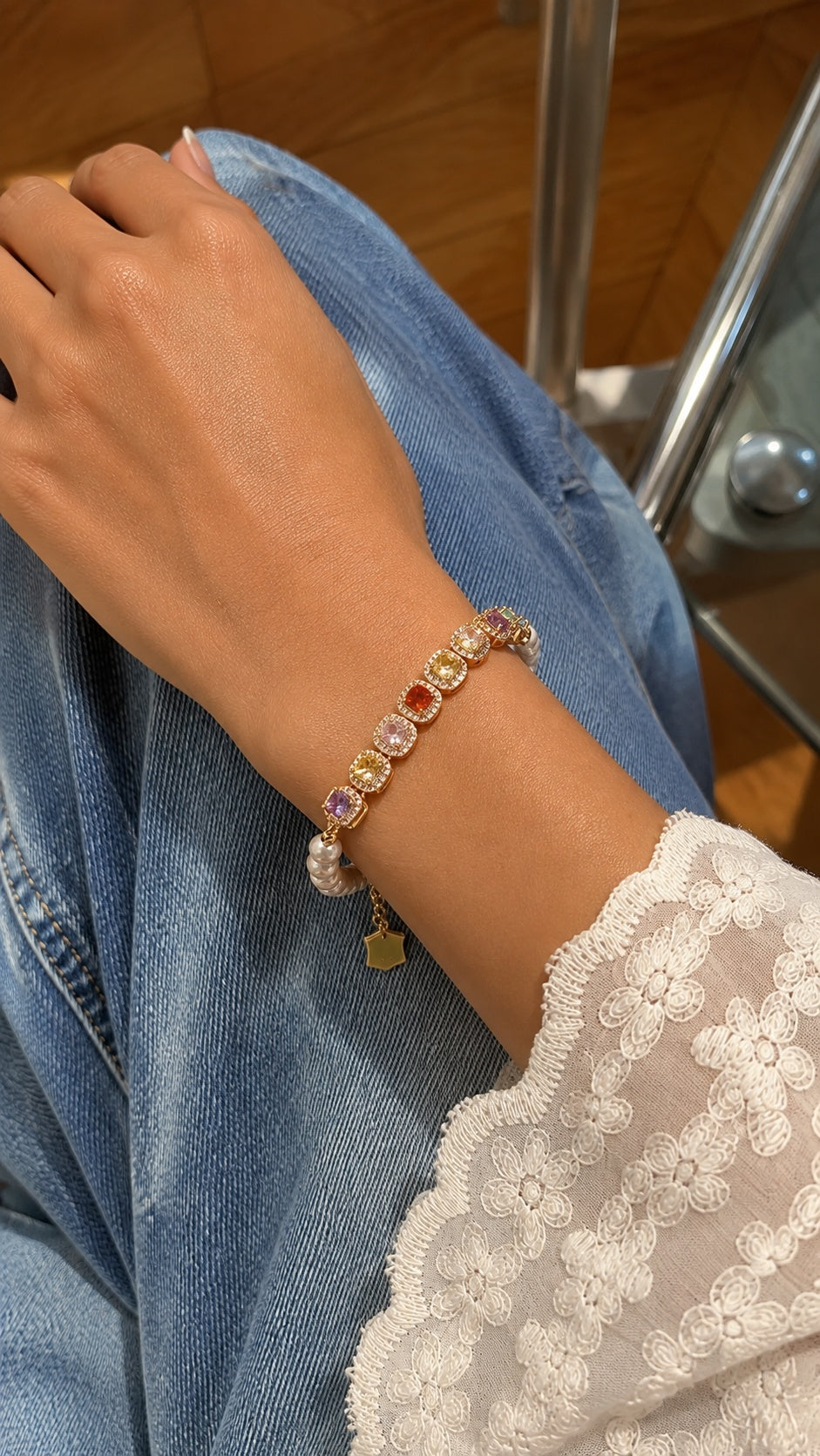 Side view of model wrist wearing colorful rainbow CZ gem pearl bracelet with lace top and jeans