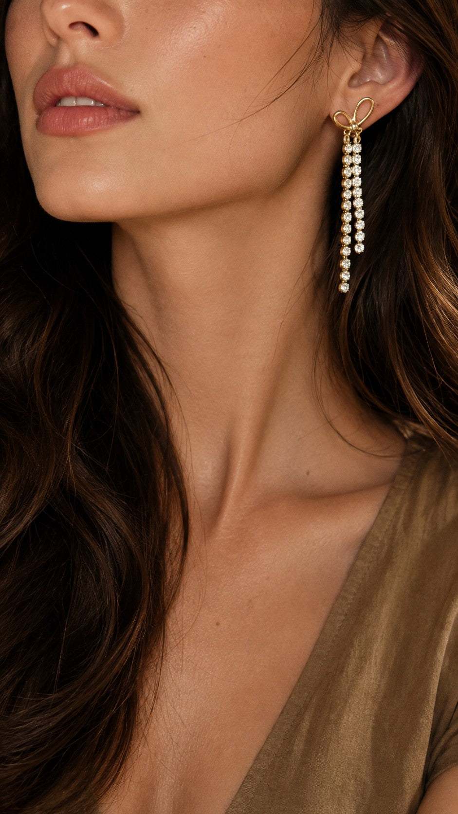 Side view close up of blonde model wearing long gold crystal bow drop earrings with white sweater