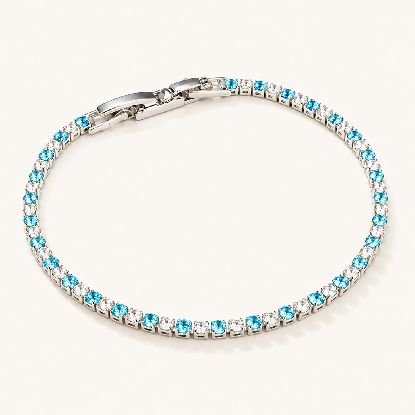 Minimalist flat lay of a white gold-tone tennis bracelet featuring alternating blue and clear zirconia on a clean white background.