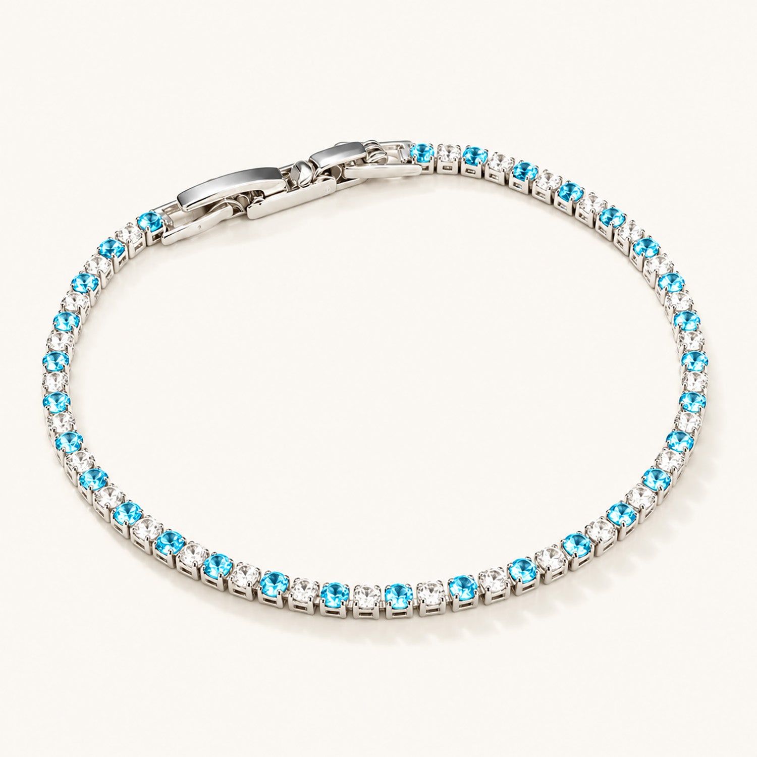 Minimalist flat lay of a white gold-tone tennis bracelet featuring alternating blue and clear zirconia on a clean white background.
