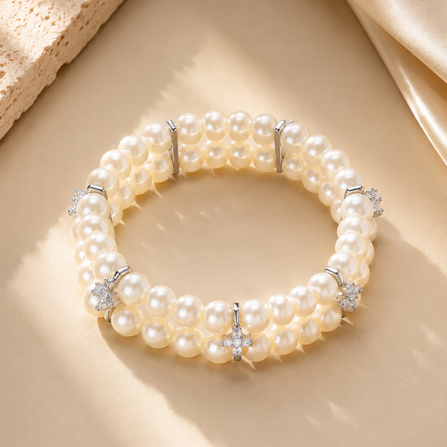 Classic double-row pearl bracelet with sparkling zirconia resting on textured stone and warm silk.