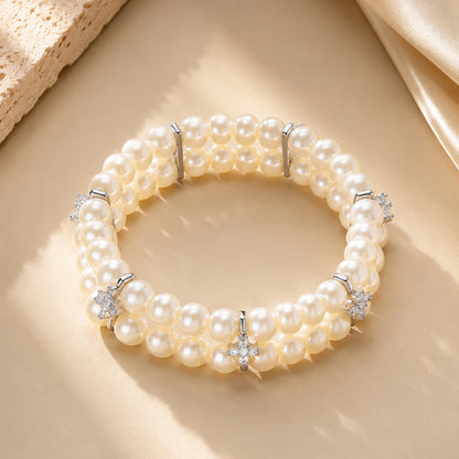 Classic double-row pearl bracelet with sparkling zirconia resting on textured stone and warm silk.